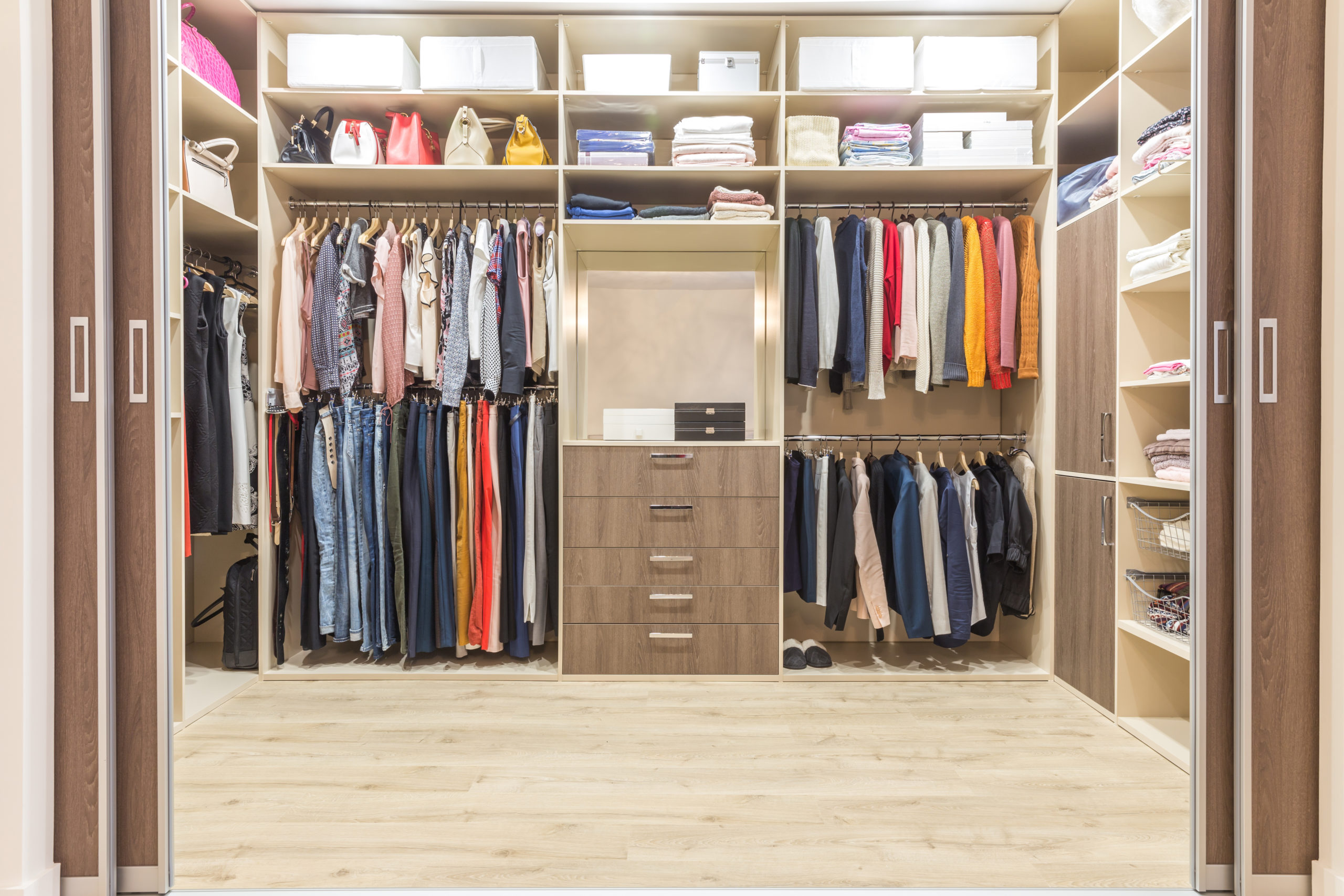 Modern wooden wardrobe with clothes hanging on rail in walk in c